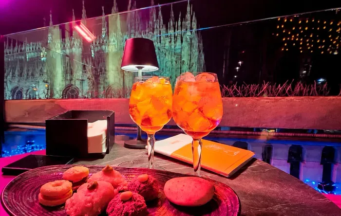 Duas taças de Aperol Spritz e doces em um terraço com vista para o Duomo de Milão à noite