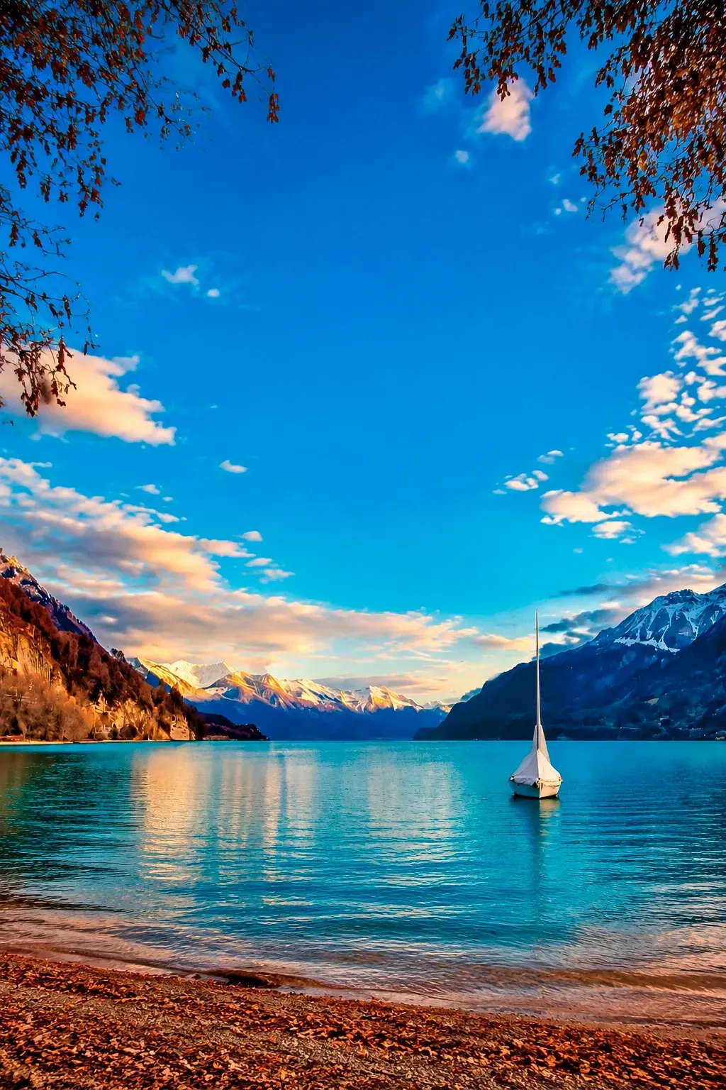 Lago azul com um veleiro e montanhas nevadas ao fundo